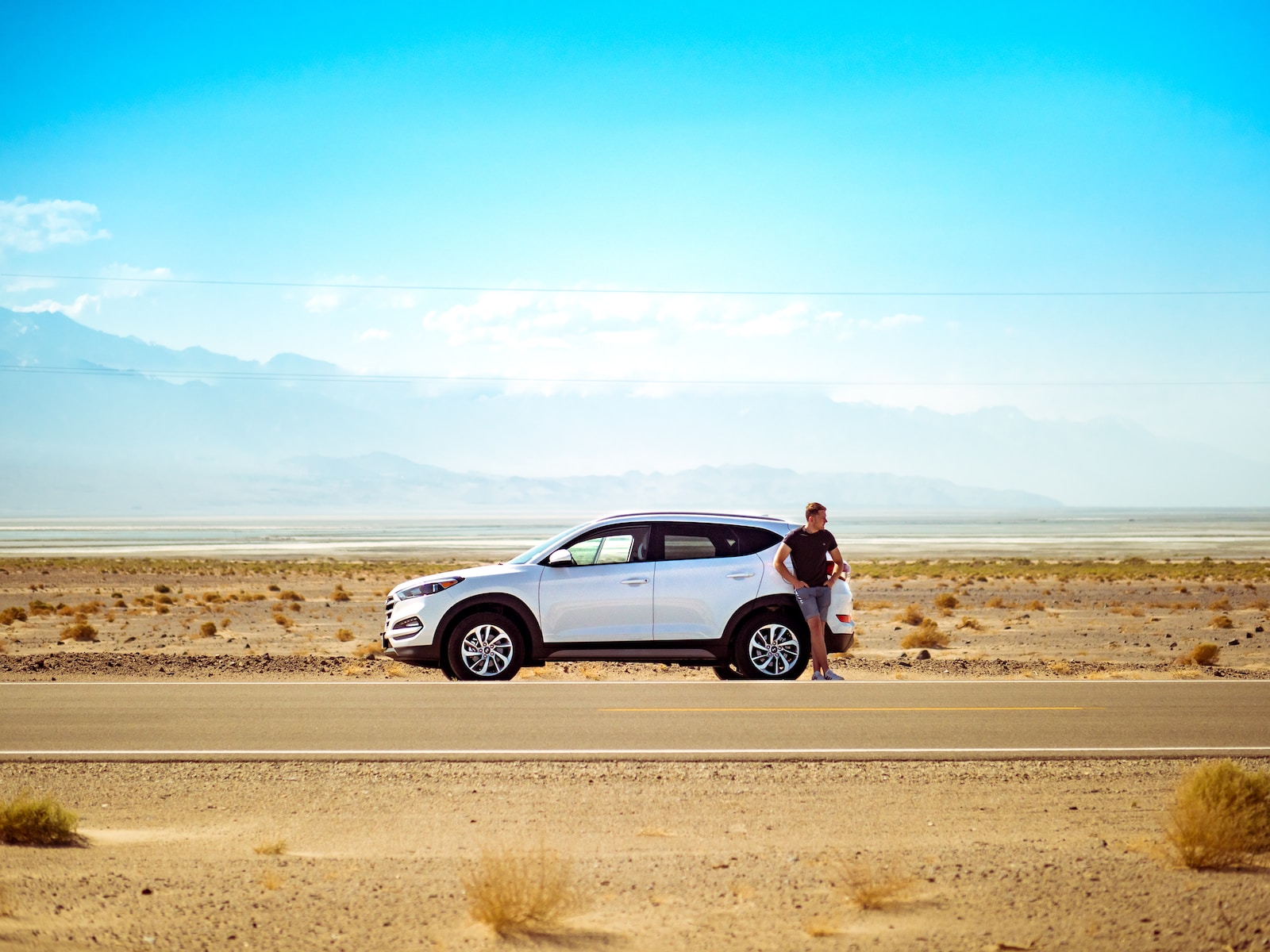 man with auto insurance standing beside white SUV near concrete road under blue sky at daytime